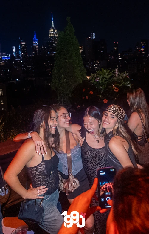 Group of friends posing with NYC skyline during Fuego Thursdays Latin rooftop party.