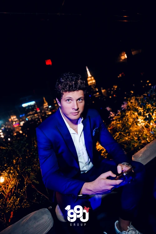 Man in blue suit enjoying the NYC skyline at Fuego Thursdays rooftop event.