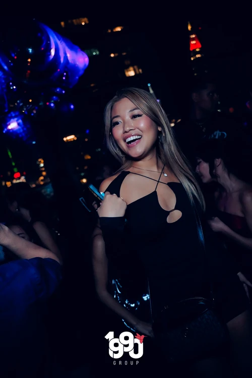 Partygoer dancing and smiling at Fuego Thursdays' rooftop party in NYC, surrounded by vibrant lights.