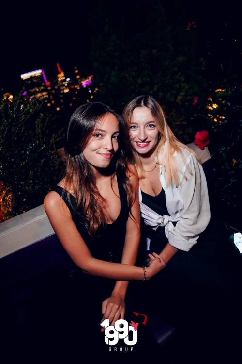 Two women smiling and enjoying the vibrant rooftop party at Fuego Thursdays with a stunning NYC skyline backdrop.