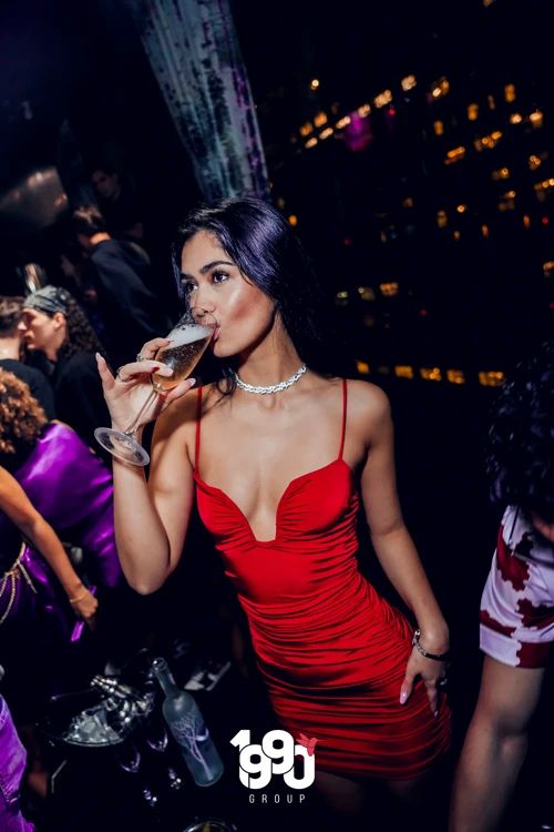 Woman in a red dress sipping champagne at Fuego Thursdays, Manhattan’s hottest Latin rooftop party.
